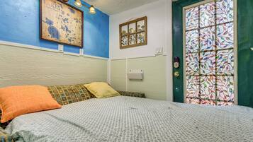 A room with a bed, a framed map on the wall, a window with a stained glass design, and a door with a keyhole.