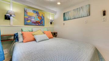 A bedroom with a bed, two wall-mounted lamps, and two abstract paintings.