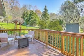A wooden deck with a table and chairs, surrounded by a wooden railing, overlooking a grassy yard with trees and a shed. - Tranquil Catskills Home w/ Creek & Fire Pits (Parksville)