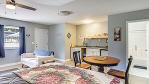 Quarto com cama, uma cadeira, uma mesa, ventilador de teto e vista para o exterior.