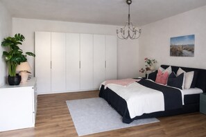 A bedroom with a bed, a wardrobe, a chandelier, a plant, and a painting on the wall. - Cozy Countryside Home With Terrace (Brezzo di Bedero)