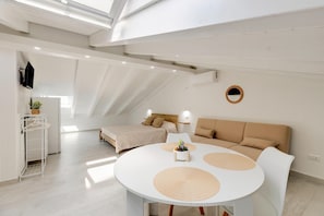 Une pièce moderne et bien éclairée, comprenant un lit, un canapé, une table à manger et une petite plante.
