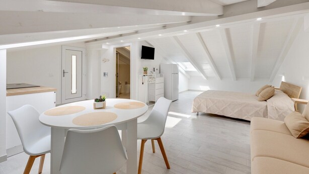 Ein modernes Schlafzimmer im Loft-Stil mit schrägem Dach, einem Bett und einem Essbereich mit Tisch und Stühlen.