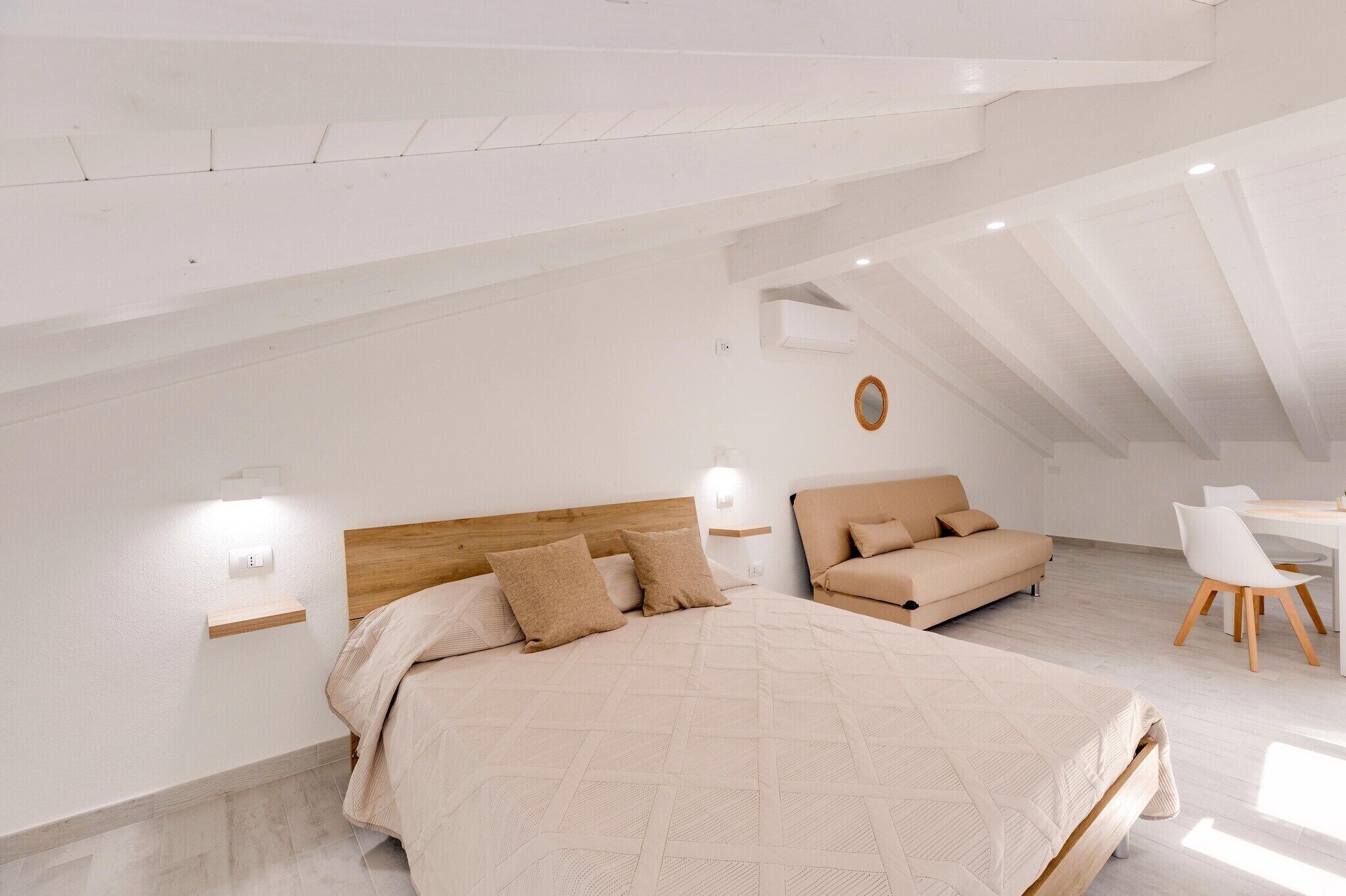 A bedroom with a large bed, a wooden headboard, a sofa, a small table, and a wall-mounted light fixture.