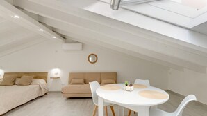 Ein modernes Schlafzimmer mit einem Bett, einem Sofa, einem Esstisch mit Stühlen und einem Oberlicht.