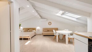 Ein modernes Loft-Schlafzimmer mit Dachfenster, einem Bett, einer Couch, einem Esstisch und einer Küchenzeile.