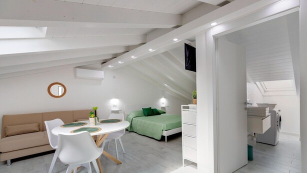 A modern, well-lit room with a dining table, chairs, a sofa, a bed, and a washing machine. - Attic studio, with air conditioning (Castelsardo)