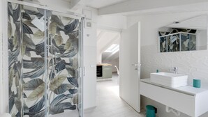 A modern bathroom with a glass shower door, a white sink, and a mirror above it. - Attic studio, with air conditioning (Castelsardo)
