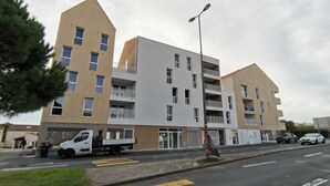 En flereetagers boligbygning med altaner, en gade foran og en hvid varevogn parkeret.
