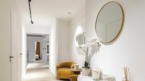 Un interior moderno con un pasillo que lleva a una habitación, un espejo redondo, una mesita pequeña y una silla.