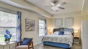 Quarto com cama, cadeira, escrivaninha, ventilador de teto e obras de arte nas paredes.