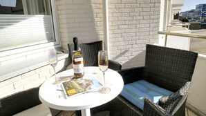 Uma varanda com uma cadeira de vime, uma mesa com garrafa de vinho e copos, e uma revista.