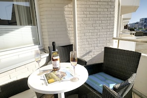 Ein Balkon mit Korbstuhl, Tisch, Weinflasche und Gläsern sowie einer Zeitschrift.