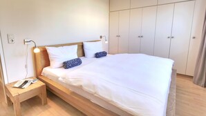 Cama bem arrumada com lençóis brancos, cabeceira de madeira e duas luminárias de cabeceira.