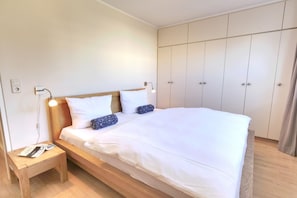 Ein ordentlich bezogenes Bett mit weißen Leinentüchern, einem Holzkopfteil und zwei Nachttischlampen.