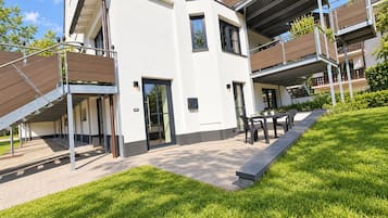 Ein modernes, mehrgeschossiges Wohngebäude mit einer überdachten Außenbereich-Sitzgelegenheit und einem gepflegten Rasen.