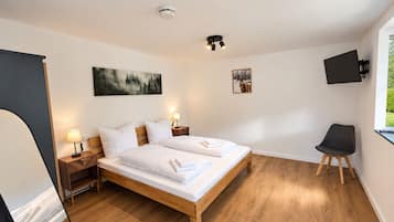 Ein Schlafzimmer mit einem hölzernen Bett, zwei Nachttischen mit Lampen, einem Wand-Fernseher und Bildern an der Wand.