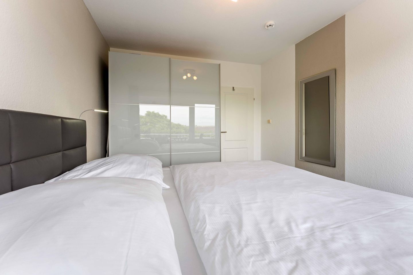 A hotel room with two beds, a large window, and a wardrobe.