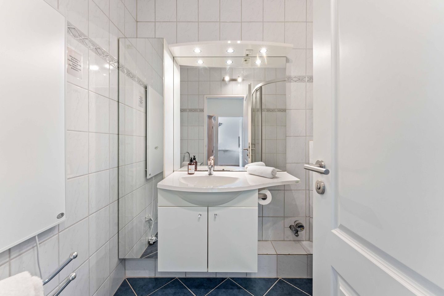 A modern bathroom with a white vanity, a mirror, a shower, and a door with a handle.
