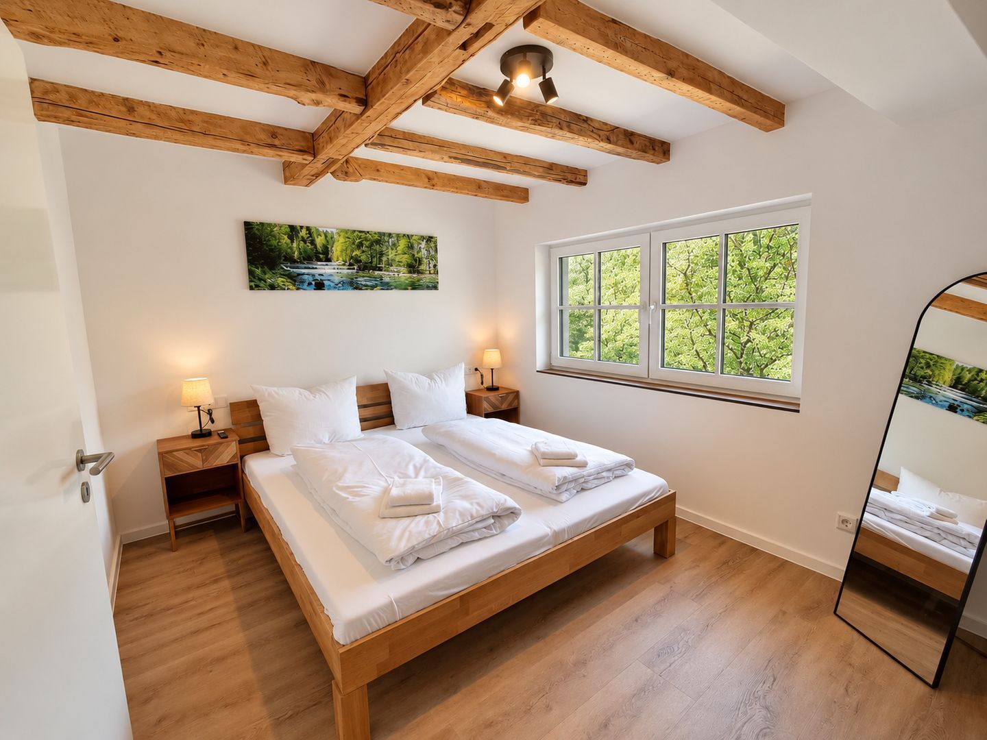 Ein Schlafzimmer mit einem Holzbett, zwei Nachttischen mit Lampen, einem Fenster mit Blick auf Grünflächen und einem Gemälde an der Wand.