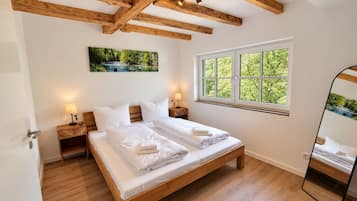 Ein Schlafzimmer mit einem Holzbett, zwei Nachttischen mit Lampen, einem Fenster mit Blick auf Grünflächen und einem Gemälde an der Wand.