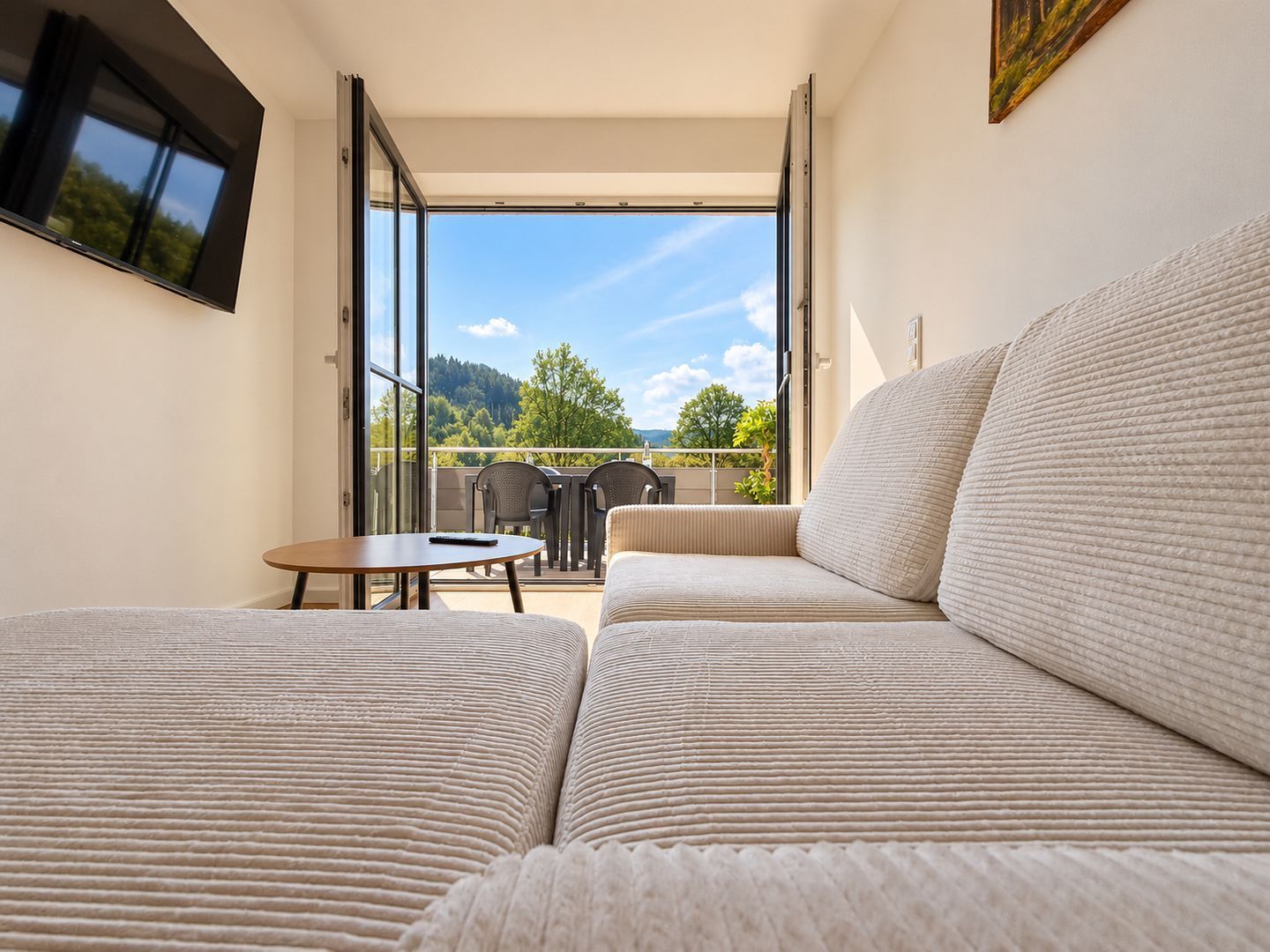 Ein modernes Zimmer mit einer Couch, einem Tisch und einem an der Wand befestigten Fernseher.