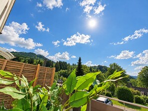 Une clôture en bois, un ciel dégagé parsemé de nuages et une vue sur une colline boisée.