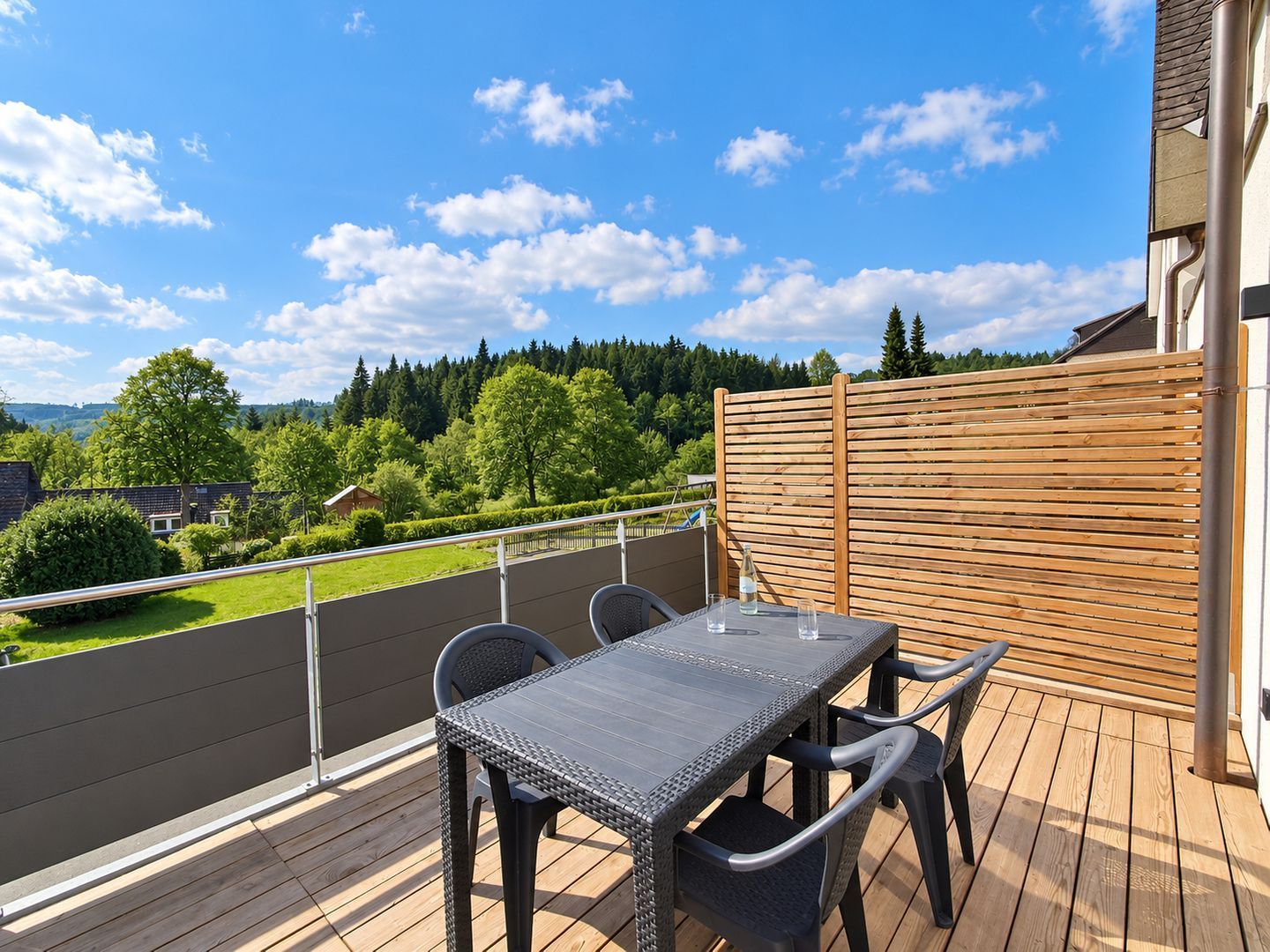 Une terrasse avec une table et des chaises, donnant sur un paysage verdoyant, avec des arbres et une maison.