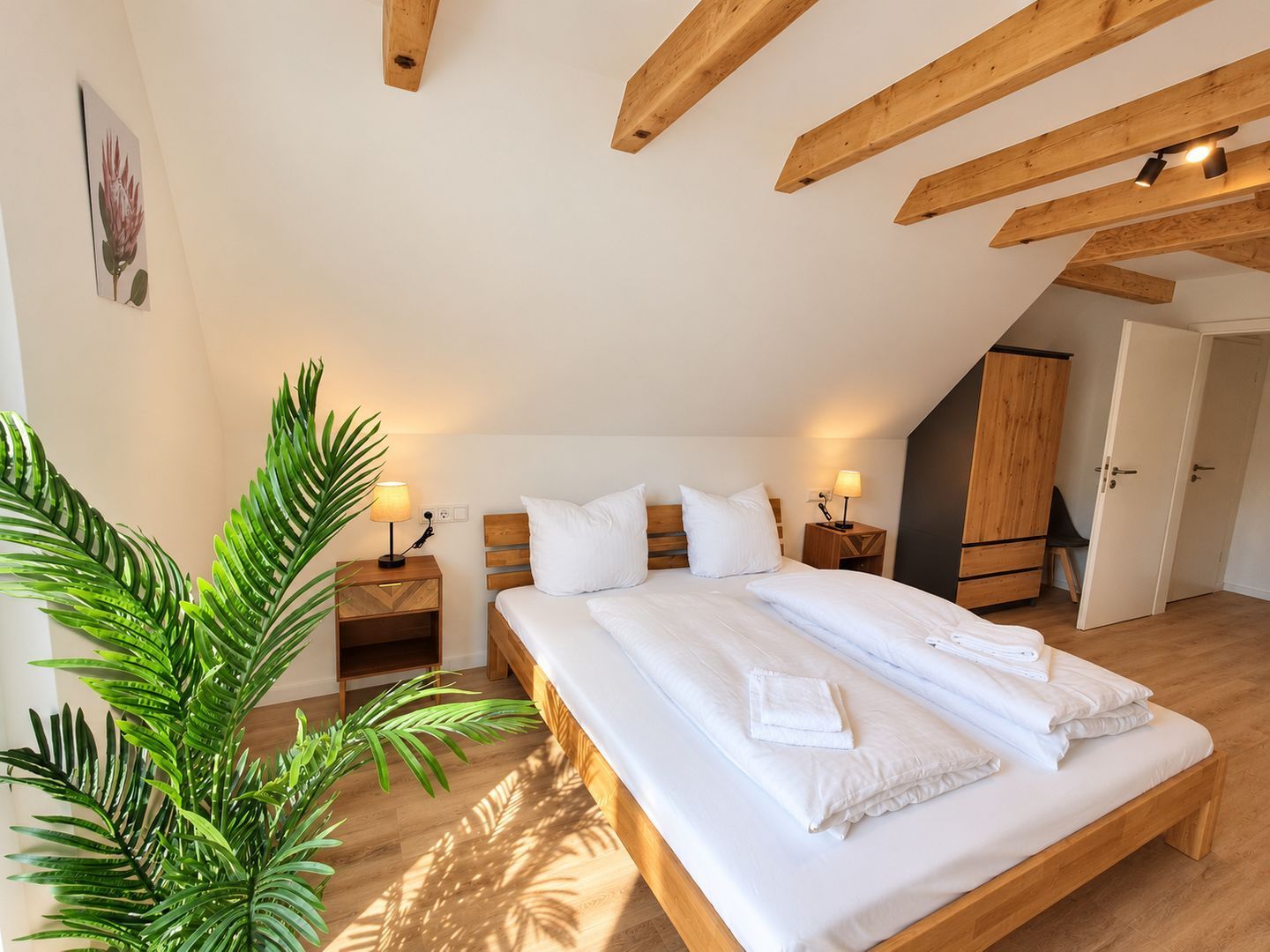 Ein Schlafzimmer mit einem großen Bett, Holzbalken, einer Pflanze und einer Tür.