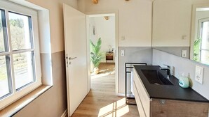Ett modernt kök med ett stort fönster, synliga träbjälkar och utsikt över en trädgård.