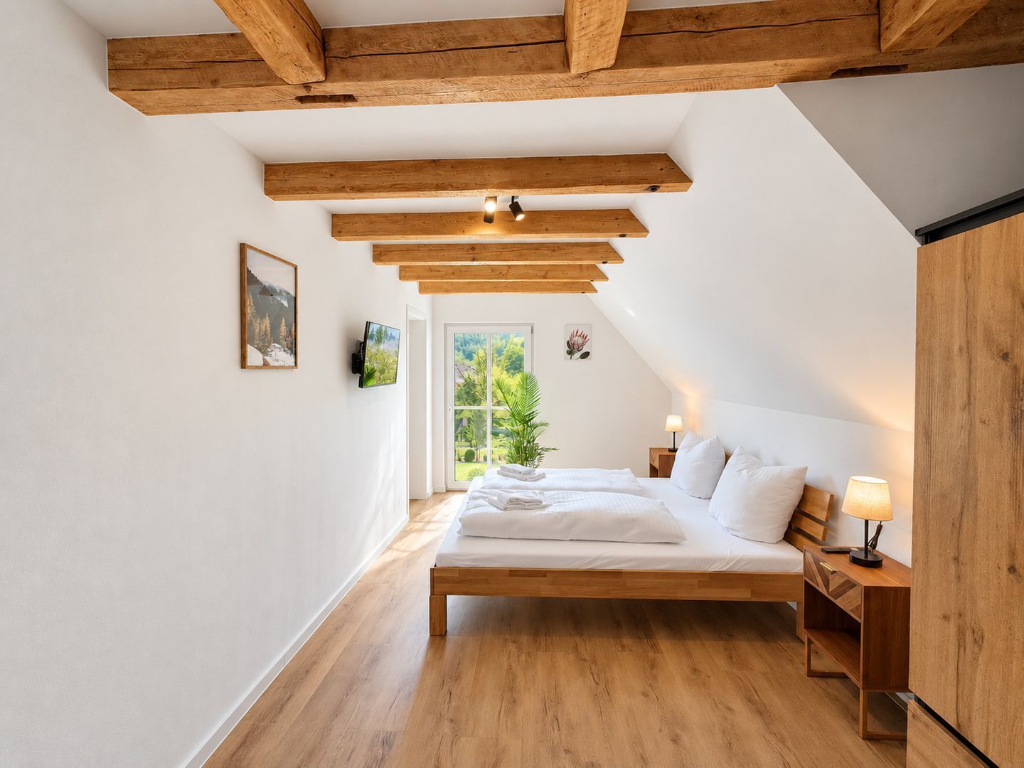Ein Schlafzimmer mit Holzbalkendecke, einem Bett mit weißen Leinen, einem Nachttisch und einem Fenster mit Blick auf Grünflächen.