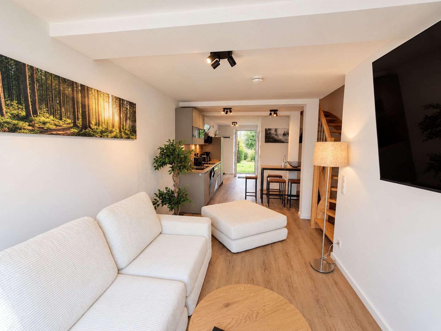 Ein modernes Wohnzimmer mit einer Couch, einem runden Couchtisch und einem Waldgemälde.