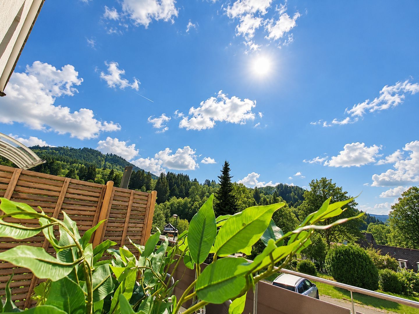 Ein Holzzaun, ein klarer Himmel mit Wolken und Blick auf einen bewaldeten Hügel.