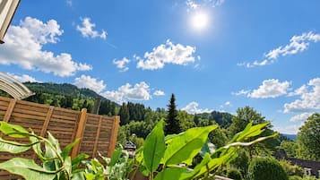 Ein Holzzaun, ein klarer Himmel mit Wolken und Blick auf einen bewaldeten Hügel.