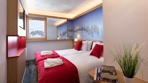 Ett hotellrum med två sängar, ett stort fönster, en tavla som föreställer ett snötäckt landskap, ett nattduksbord med en växt och en spegel.