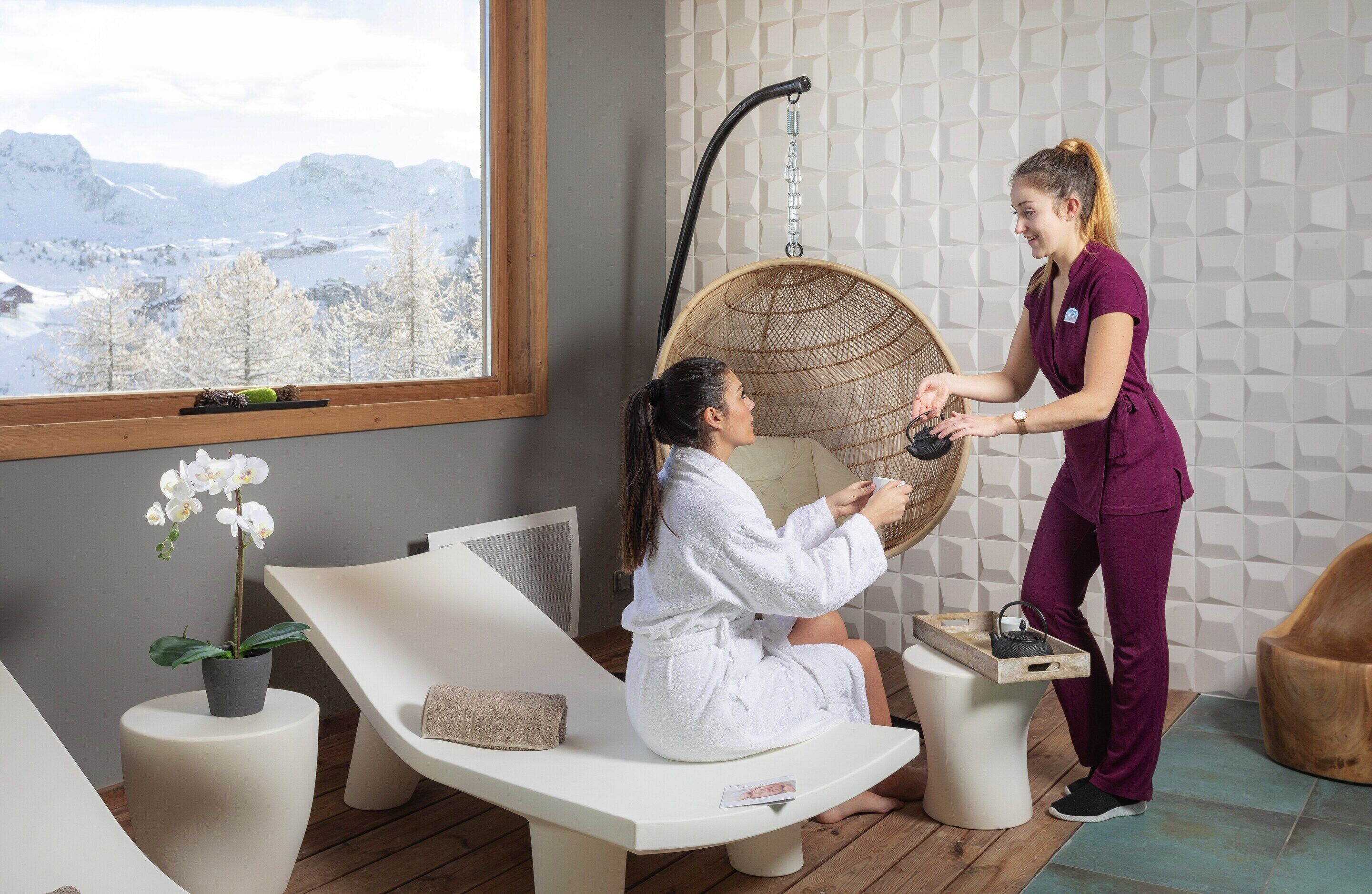 Une salle de spa équipée d’un fauteuil de massage, d’une table de massage, d’une fenêtre donnant sur les montagnes et d’une orchidée en pot.