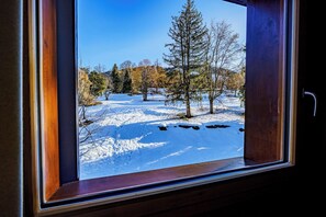 Ein Fenster mit Blick auf eine verschneite Landschaft, Bäume und einen klaren Himmel.
