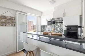 Eine moderne Küche mit schwarzer Arbeitsplatte, weißen Schränken, einer Mikrowelle, einer Kaffeemaschine und Blick ins Freie.