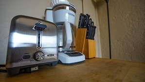 Une cuisine équipée d’un grille-pain, d’une machine à café et d’un bloc à couteaux, le tout posé sur un plan de travail en bois.
