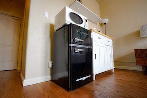 Una cocina compacta con un refrigerador negro, un microondas y un armario blanco.