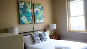Une chambre d’hôtel avec un lit, deux tableaux accrochés au mur, une lampe de chevet et une fenêtre.