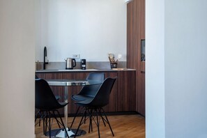 Ett kompakt kök med matplats, inrett i modern stil med ett träskåp, en kaffebryggare i rostfritt stål och två svarta stolar.