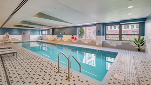 Una piscina interior con suelo de baldosas, una escalera de piscina y vistas al exterior.