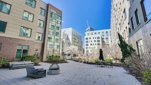 Un patio con mobiliario, una fuente de agua y edificios modernos al fondo.