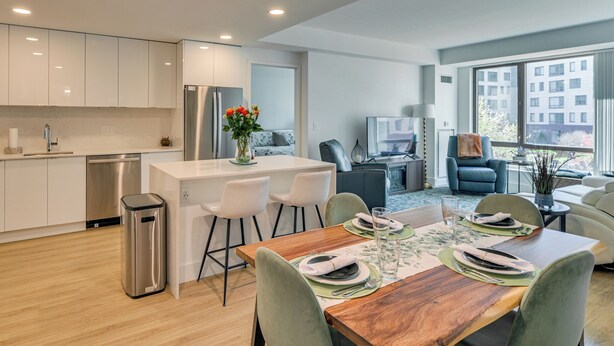 Una cocina moderna con armarios blancos, un refrigerador de acero inoxidable y un comedor con una mesa de madera dispuesta para cuatro.