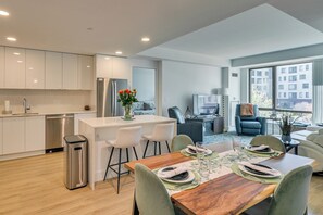 Una cocina moderna con armarios blancos, un refrigerador de acero inoxidable y un comedor con una mesa de madera dispuesta para cuatro.