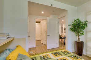 Een slaapkamer met een bed, nachtkastje, een potplant en een open deur naar een eetruimte.