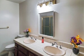 A bathroom with two sinks, a toilet, a mirror, and wall-mounted lights. - < 1 Mi to UC Riverside! Extended Base for Families (Riverside)