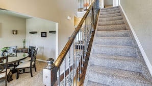 Un escalier avec une rampe en bois et des balustrades en métal, des marches recouvertes de moquette et un coin repas avec une table ronde et des chaises.