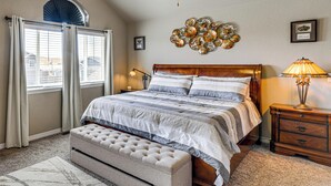 Une chambre à coucher comprenant un lit, un banc, une table de chevet, une lampe, un ventilateur de plafond et un élément décoratif mural.